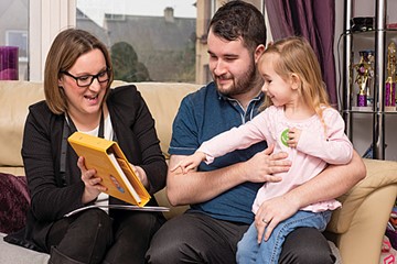 A father and toddler daughter, a girl sitting with two adults, a health visitor.